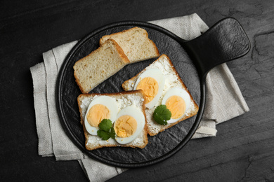 Photo of Tasty sandwiches with boiled eggs served on black table, flat lay