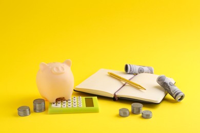 Photo of Financial savings. Piggy bank, money, calculator and stationery on yellow background