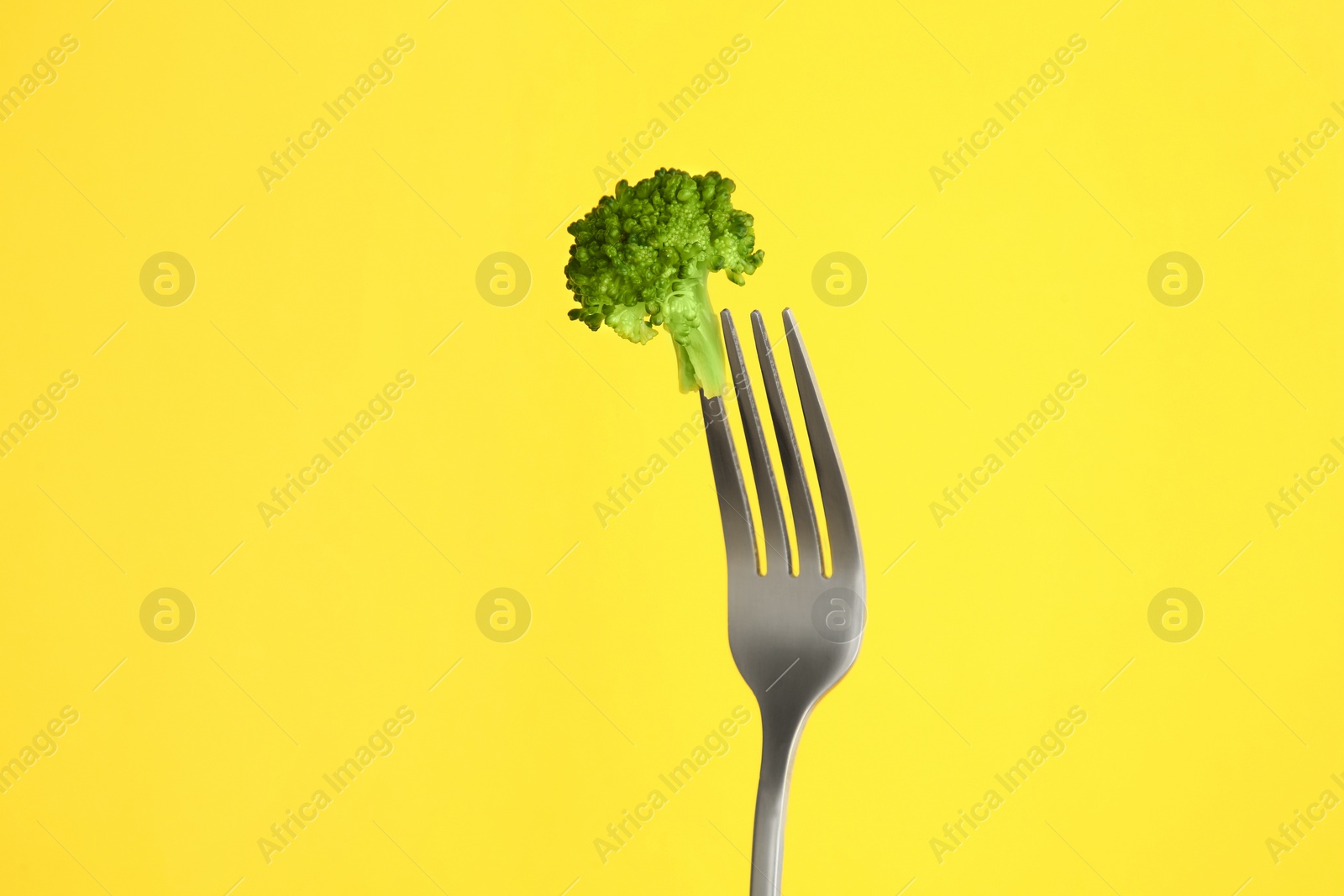Photo of Fork with tasty broccoli on yellow background