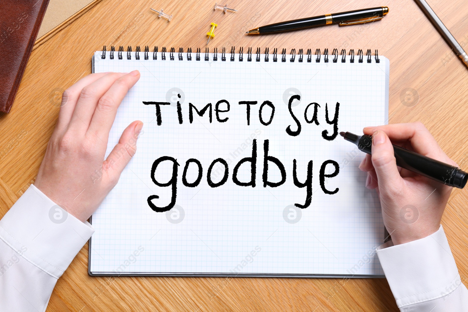 Image of Woman writing phrase Time to say Goodbye at wooden table, top view