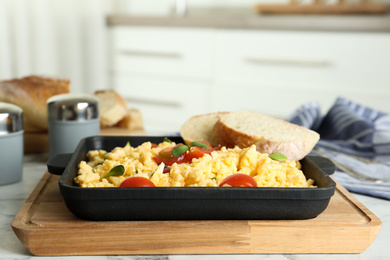 Tasty scrambled eggs with sprouts, cherry tomato and bread in frying pan on table