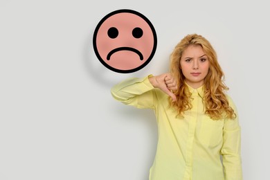 Image of Complaint. Dissatisfied woman showing thumbs-down on white background. Illustration of sad face near her