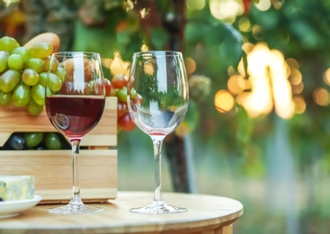 Photo of Wineglasses and crate with grapes on wooden table in vineyard