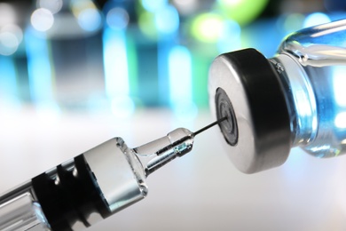 Photo of Filling syringe with vaccine from vial on blurred background, closeup