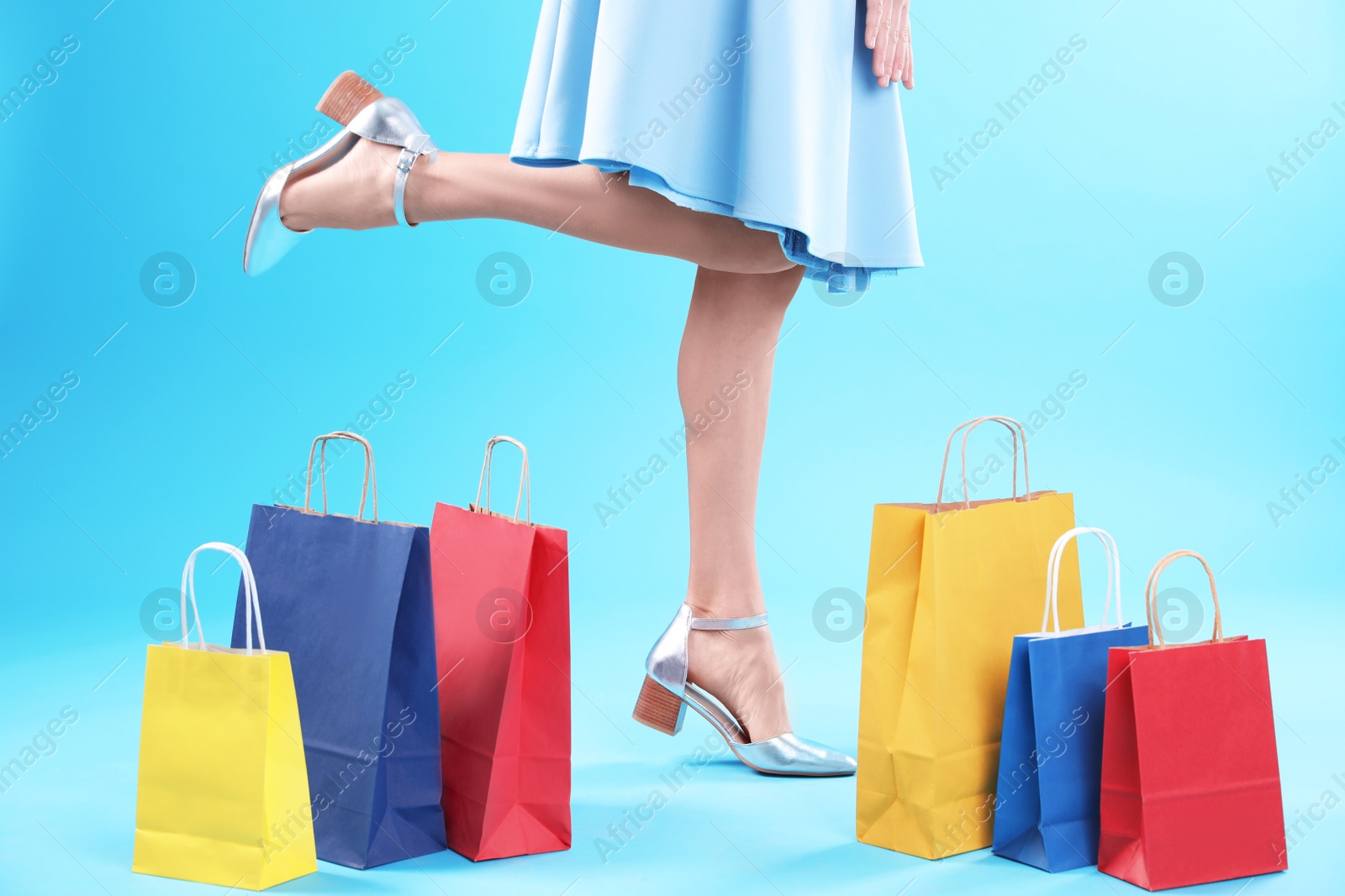 Photo of Young woman with shopping bags on color background, closeup of legs