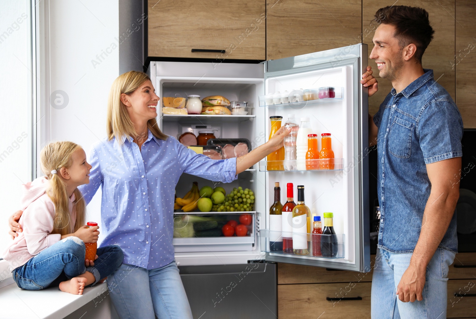 Photo of Happy family near refrigerator full of products in kitchen
