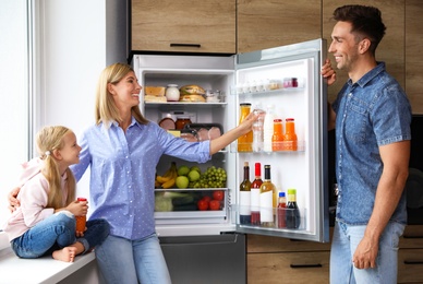 Photo of Happy family near refrigerator full of products in kitchen