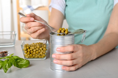 Photo of Young woman with canned green peas at table