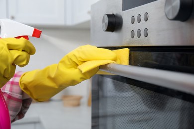 Photo of Woman cleaning oven with rag and detergent indoors, closeup
