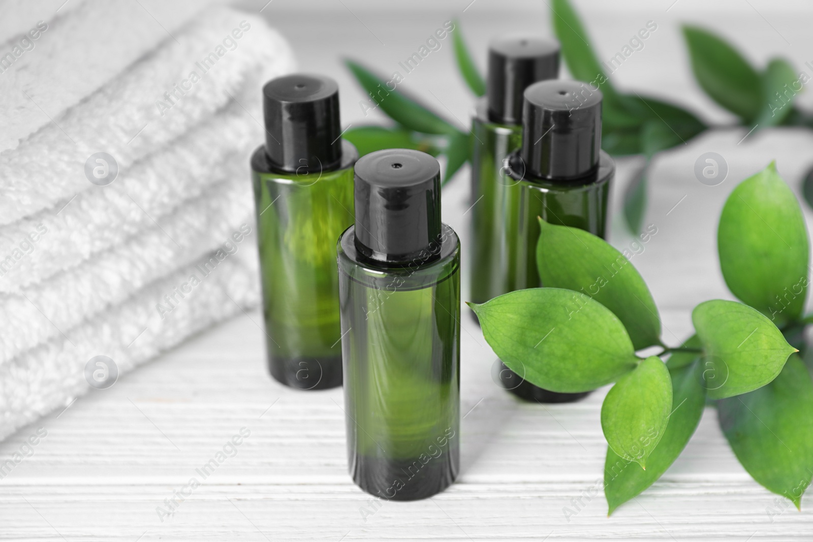 Photo of Mini bottles with cosmetic products and towels on white wooden table