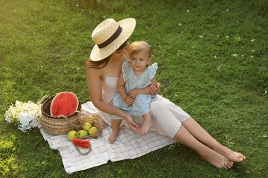 Mother with her baby daughter having picnic on green grass outdoors