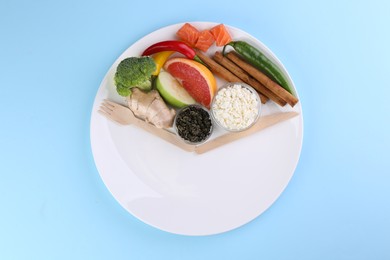 Photo of Metabolism. Plate with different food products and wooden cutlery on light blue background, top view