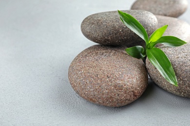 Photo of Pile of spa stones and green leaves on grey table, space for text