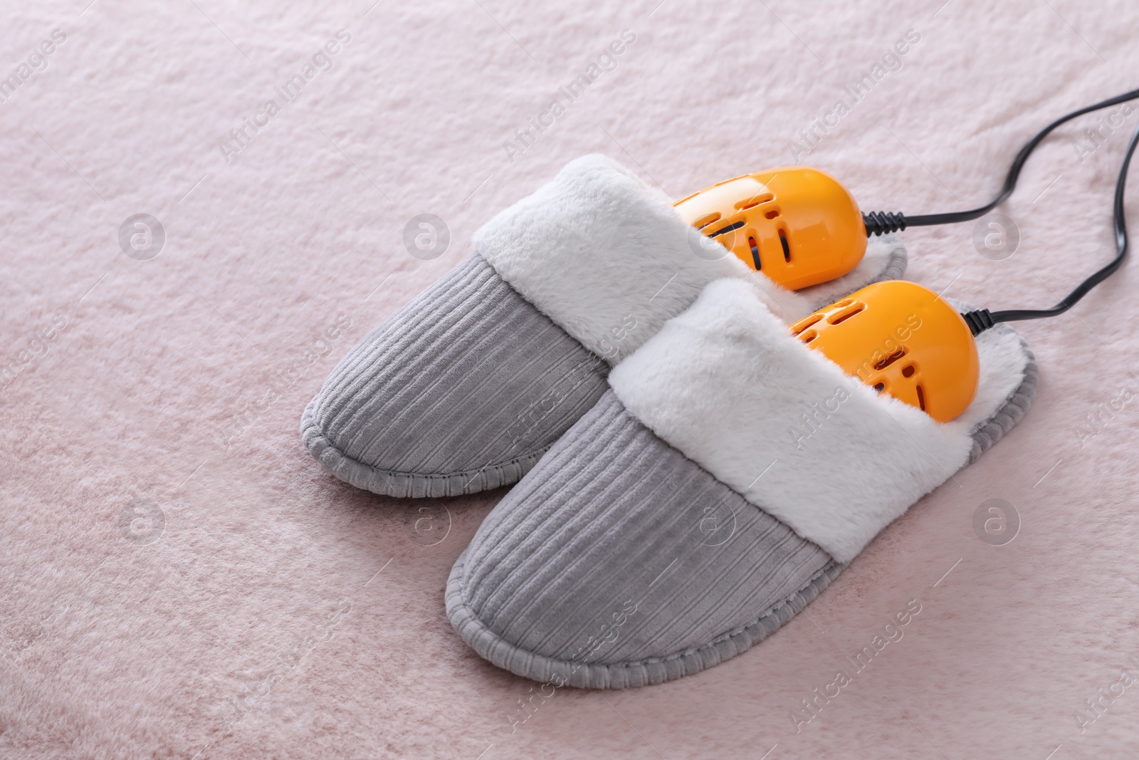 Photo of Pair of soft slippers with modern electric footwear dryer on pink carpet
