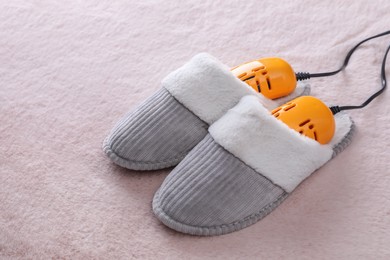 Pair of soft slippers with modern electric footwear dryer on pink carpet