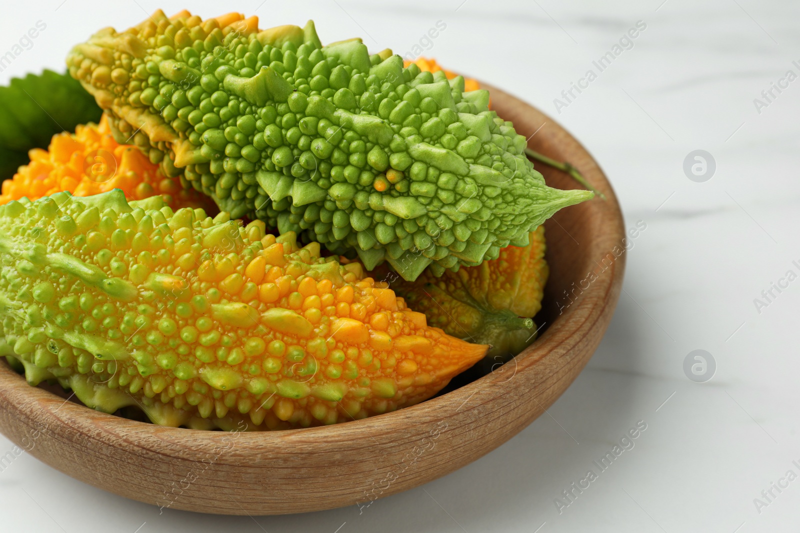 Photo of Wooden bowl with fresh bitter melons on white marble table, closeup