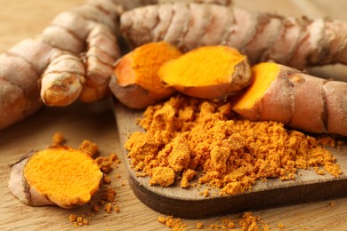 Photo of Aromatic turmeric powder and raw roots on wooden table, closeup