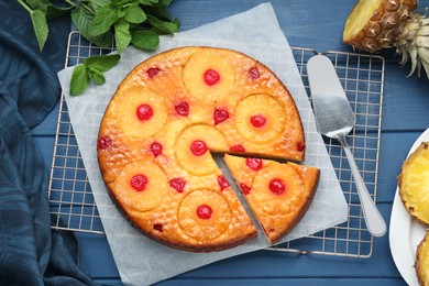 Photo of Delicious cut pineapple pie with cherry and mint on blue wooden table, flat lay