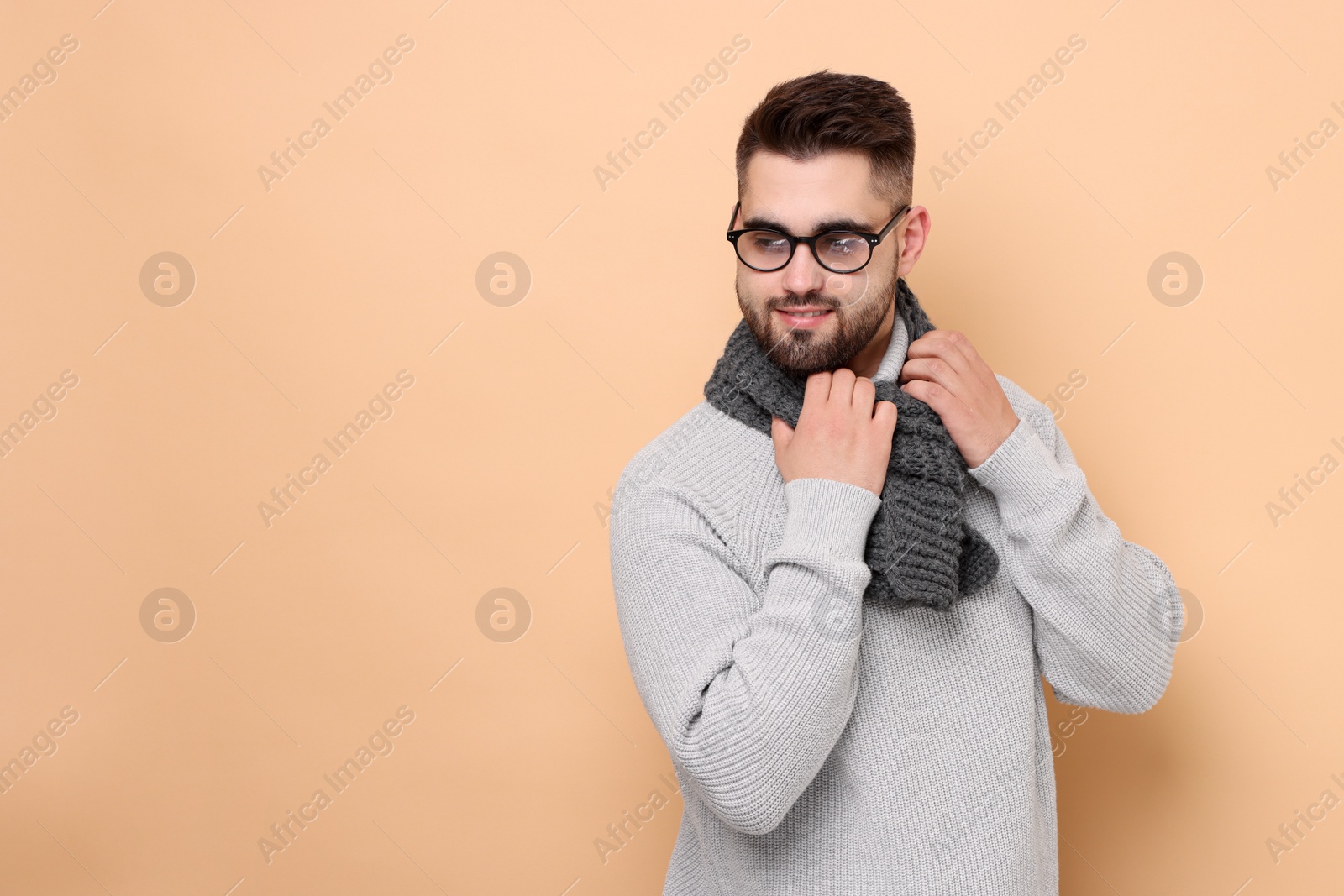 Photo of Handsome man in knitted scarf on beige background. Space for text