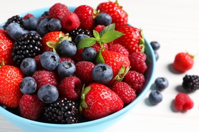 Photo of Many different fresh ripe berries in bowl on white wooden table, closeup