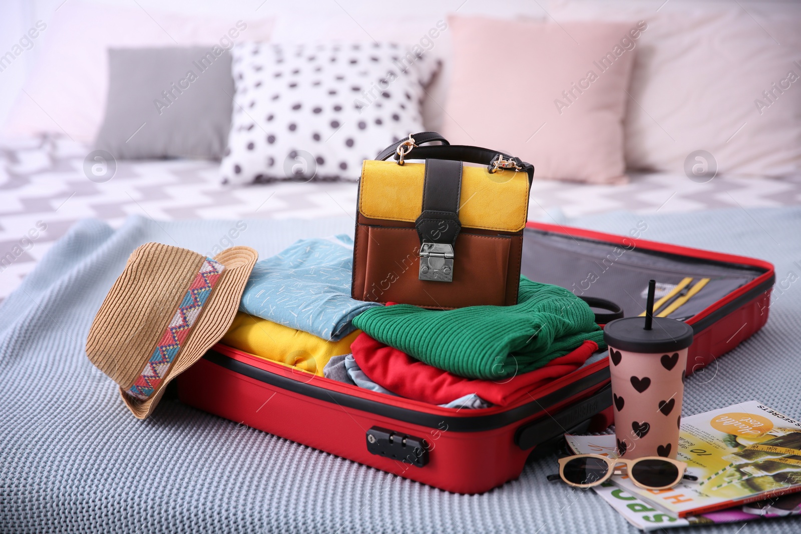Photo of Open suitcase with different personal stuff on bed