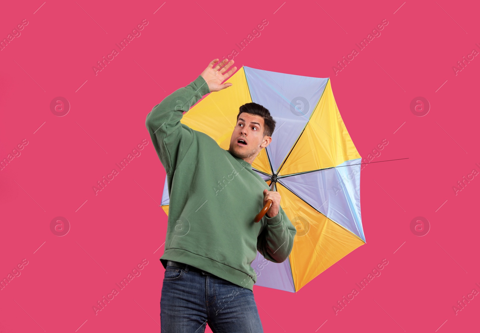 Photo of Emotional man with umbrella caught in gust of wind on pink background