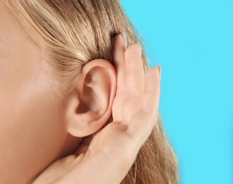 Photo of Young woman with hearing problem on color background, closeup