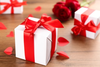 Beautiful gift box and paper hearts on wooden table, closeup. Valentine's Day celebration