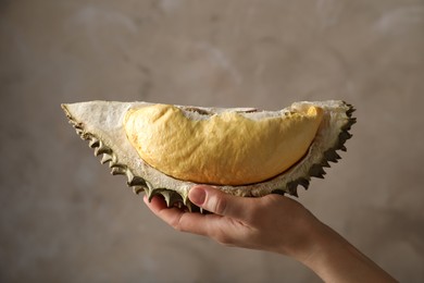 Photo of Woman holding piece of ripe durian fruit on grey background, closeup