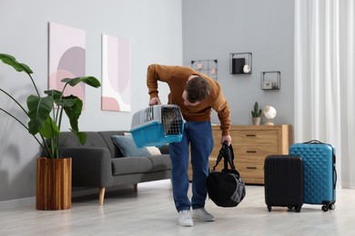 Photo of Travel with pet. Man holding carrier with cute cat and bag at home