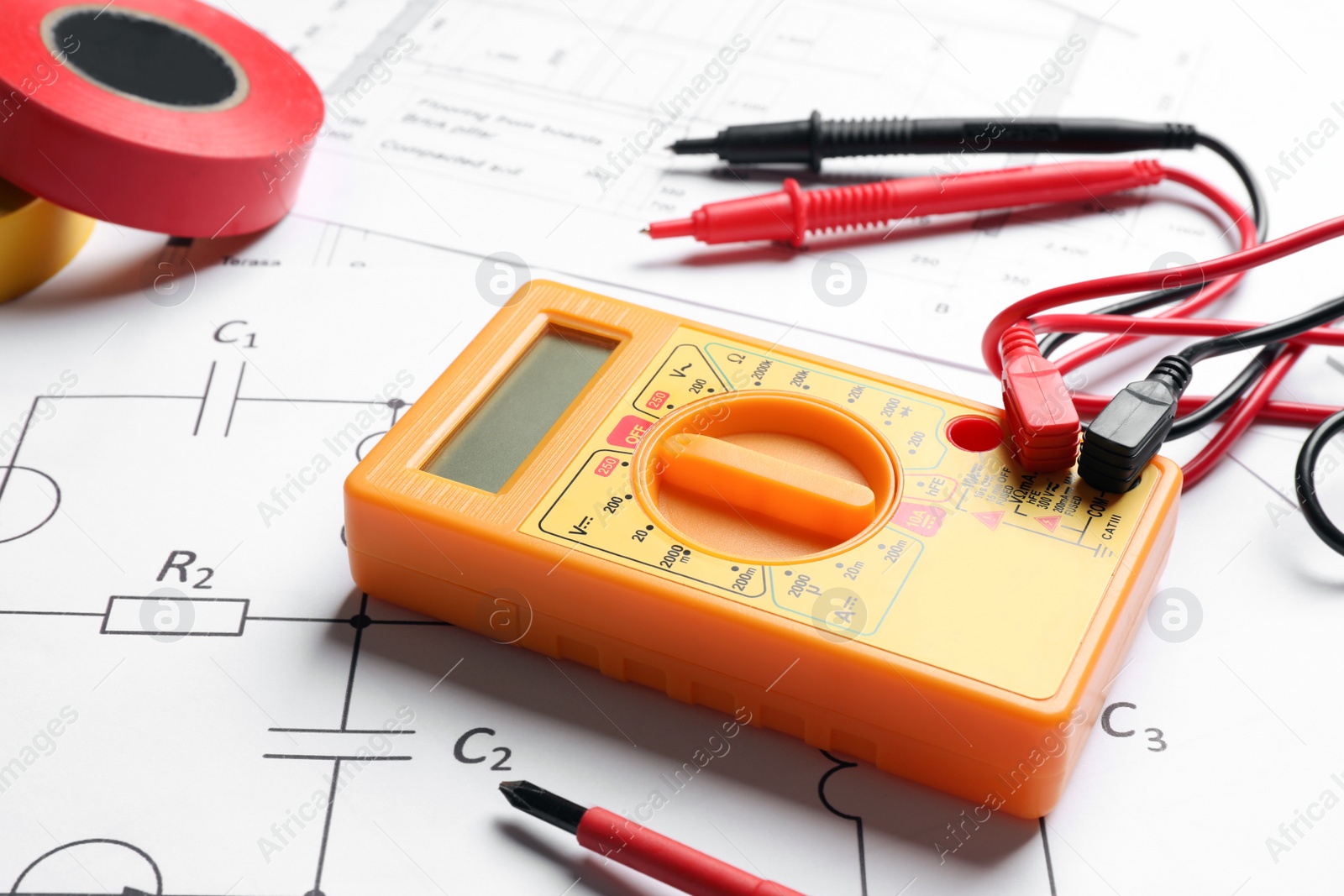 Photo of Digital multimeter and tapes on paper sheets, closeup. Electrician's supplies