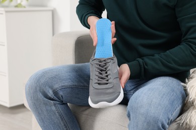 Man putting orthopedic insole into shoe indoors, closeup