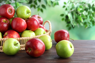 Photo of Juicy red and green apples in wicker tray on wooden table outdoors