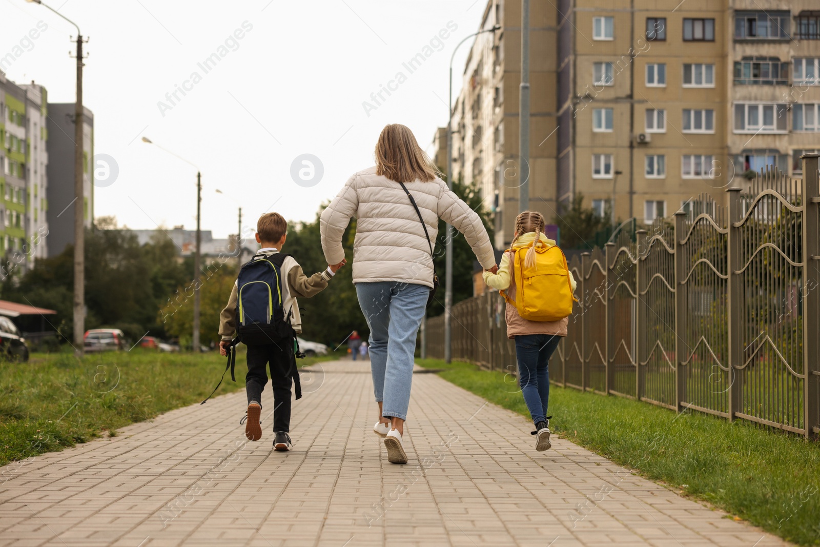 Photo of Being late for school. Senior woman and her grandchildren with backpacks running outdoors, back view