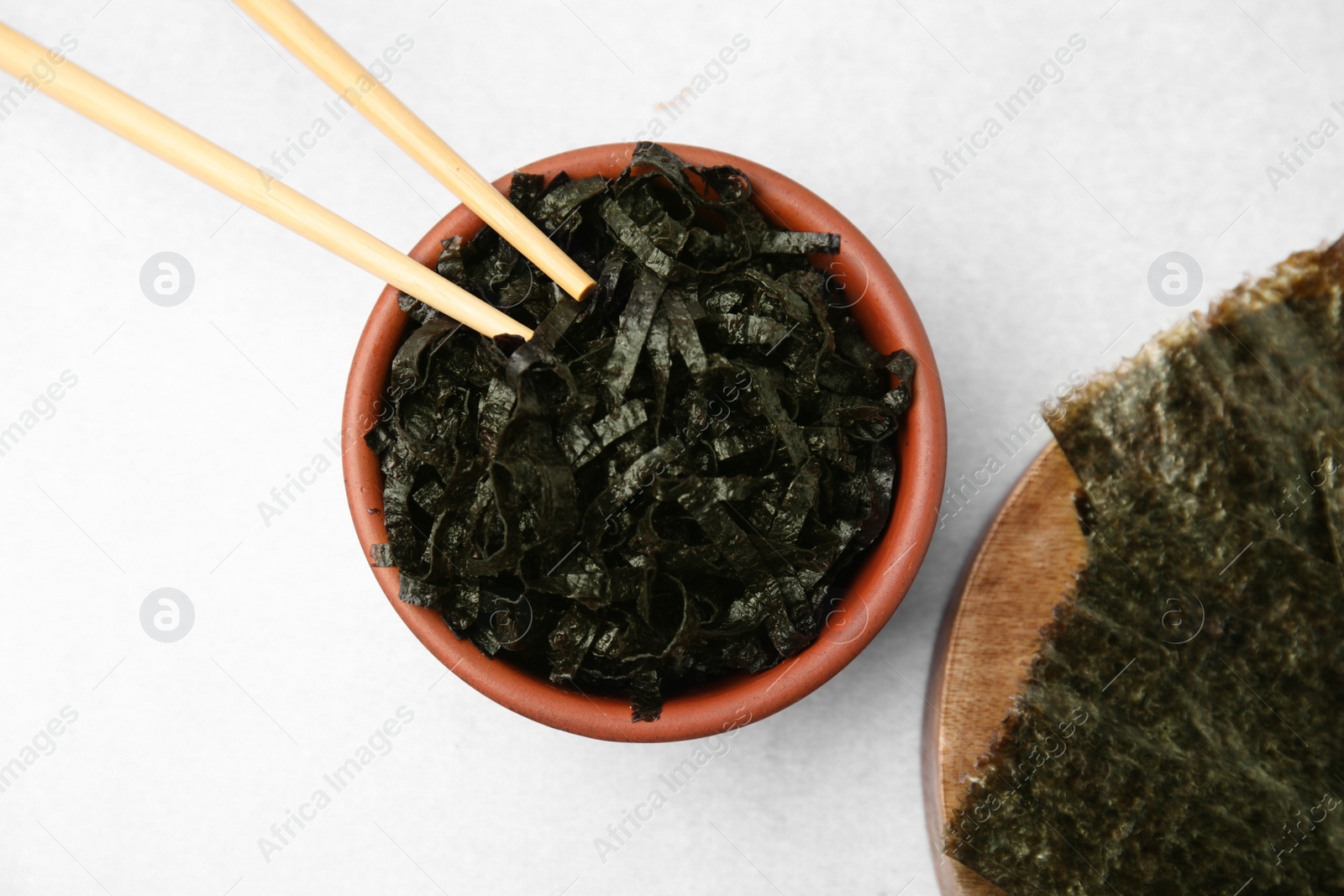 Photo of Bowl with chopped nori sheets and chopsticks on white table, flat lay