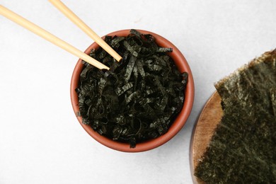 Bowl with chopped nori sheets and chopsticks on white table, flat lay