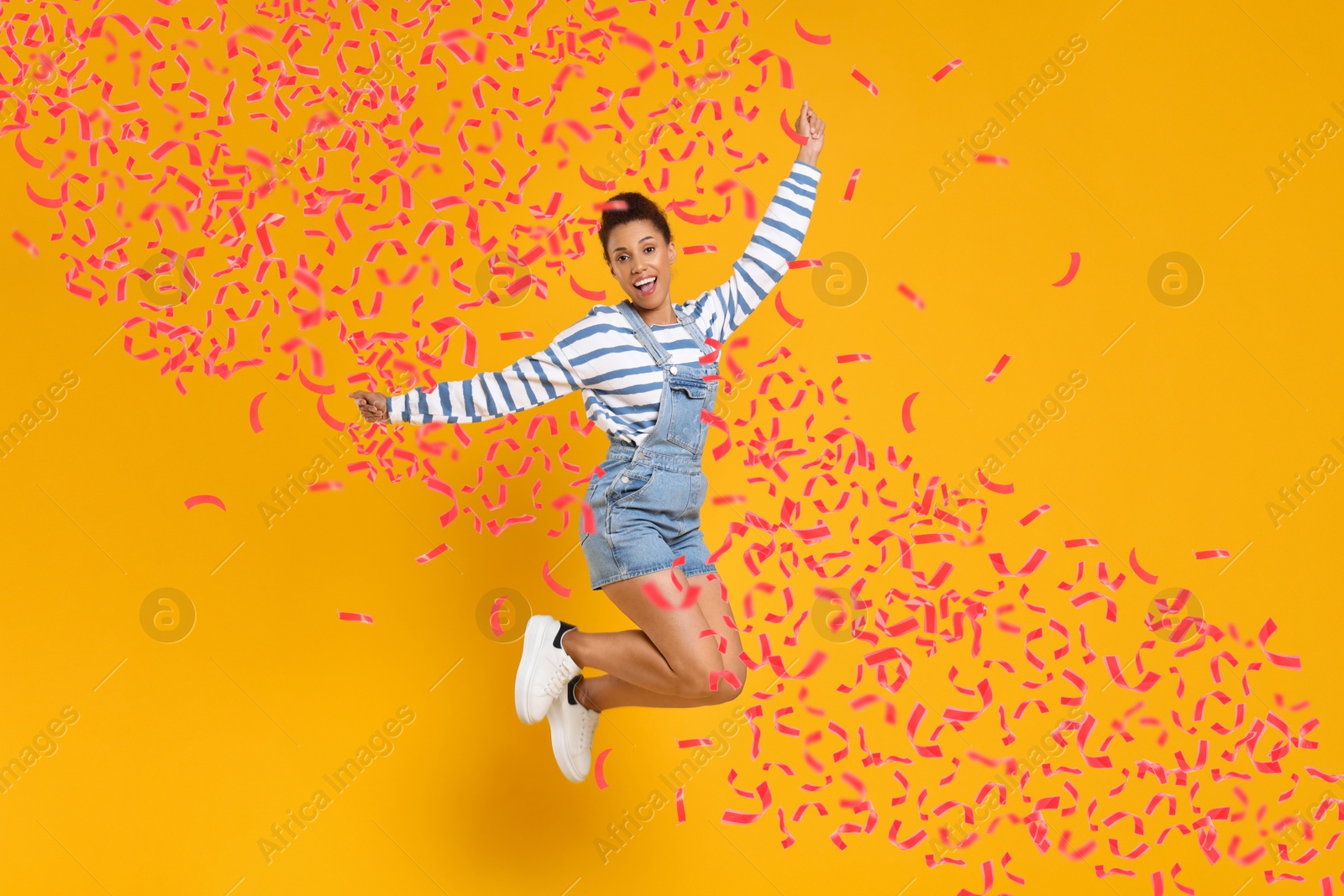 Image of Happy woman jumping under flying confetti on orange background