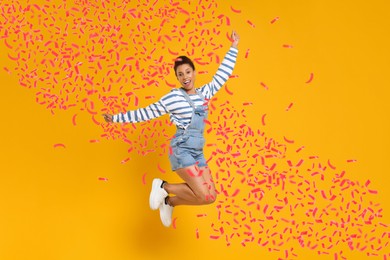 Happy woman jumping under flying confetti on orange background