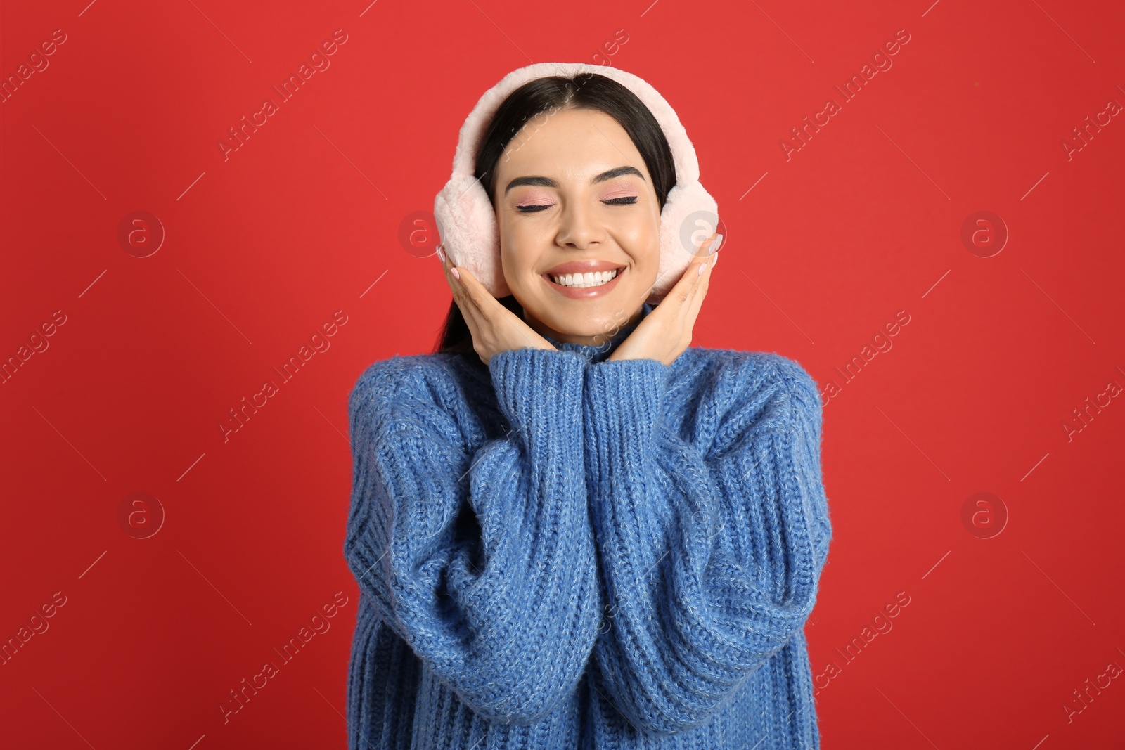 Photo of Beautiful young woman wearing earmuffs on red background