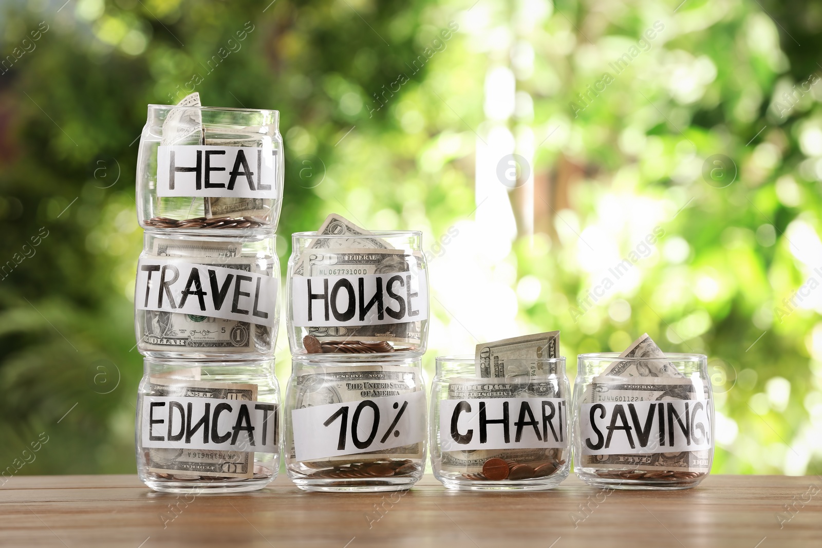 Photo of Glass jars with money for different needs on table against blurred background