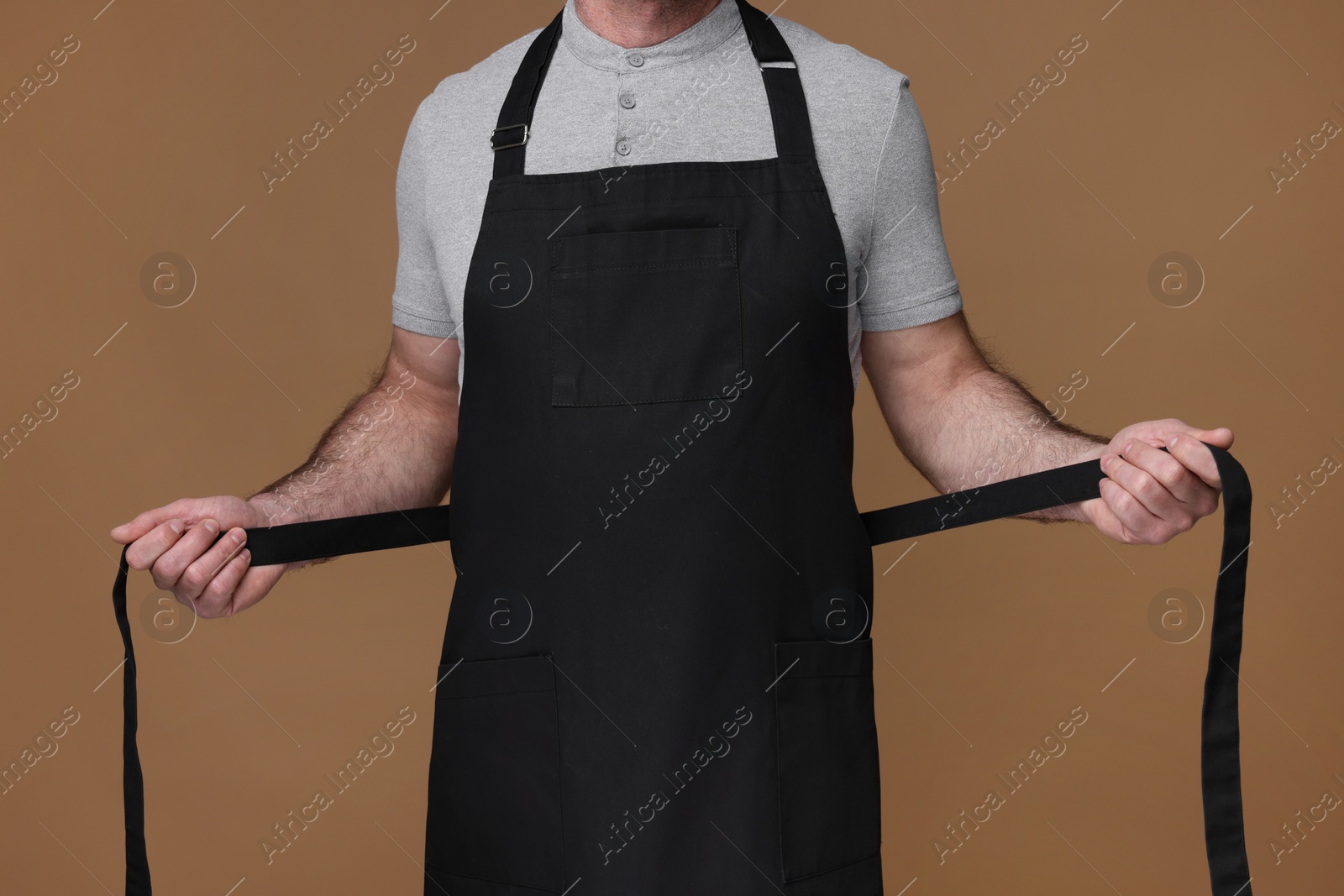 Photo of Man wearing kitchen apron on brown background, closeup. Mockup for design