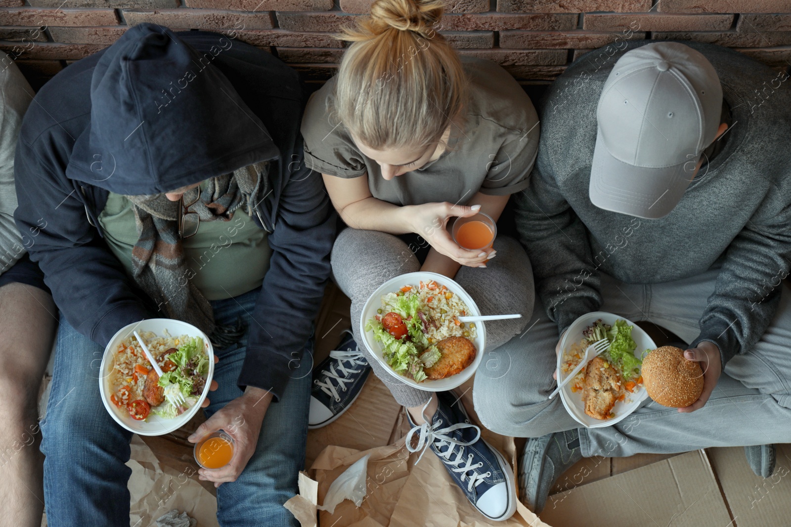 Photo of Poor people with plates of food sitting at wall indoors, view from above