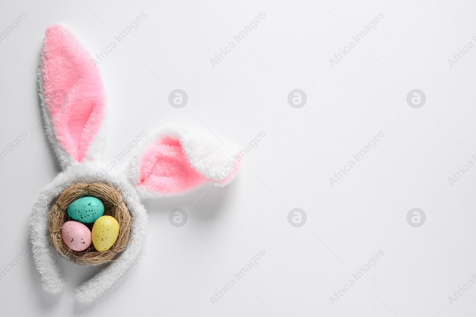 Photo of Headband with bunny ears and painted eggs on white background, top view. Easter holiday