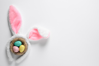 Photo of Headband with bunny ears and painted eggs on white background, top view. Easter holiday