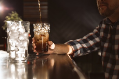 Man with glass of refreshing cola at bar counter, closeup. Pouring beverage