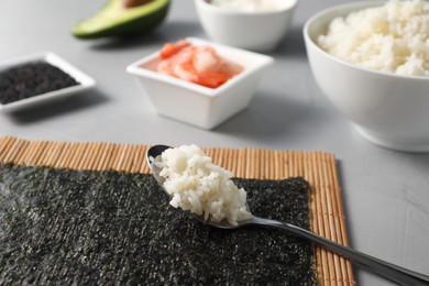Photo of Nori, spoon with rice and other ingredients for sushi on grey table, closeup
