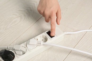 Woman pressing power button of extension cord on floor, closeup. Electrician's professional equipment