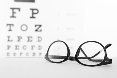 Photo of Glasses with corrective lenses on table against eye chart