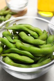 Photo of Bowl with green edamame beans in pods on light grey table, closeup