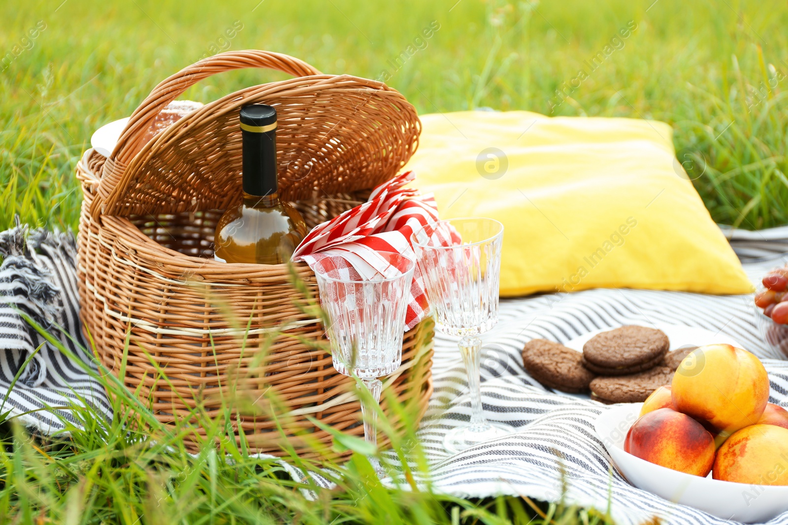 Photo of Wicker picnic basket with wine and glasses on blanket outdoors